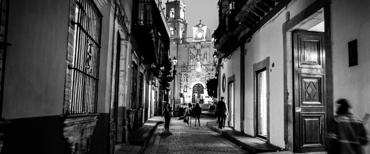 Empty city street at night, dimly lit by streetlamps.