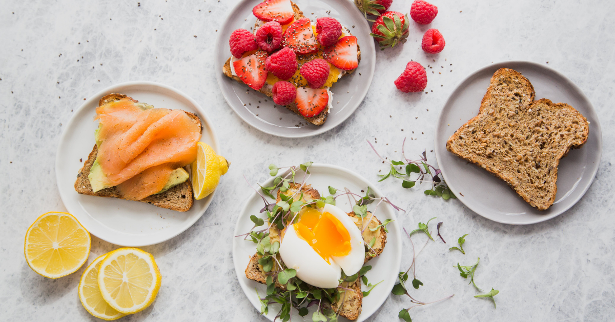 Breakfast spread of bread, strawberries, fruit, and eggs on plates.