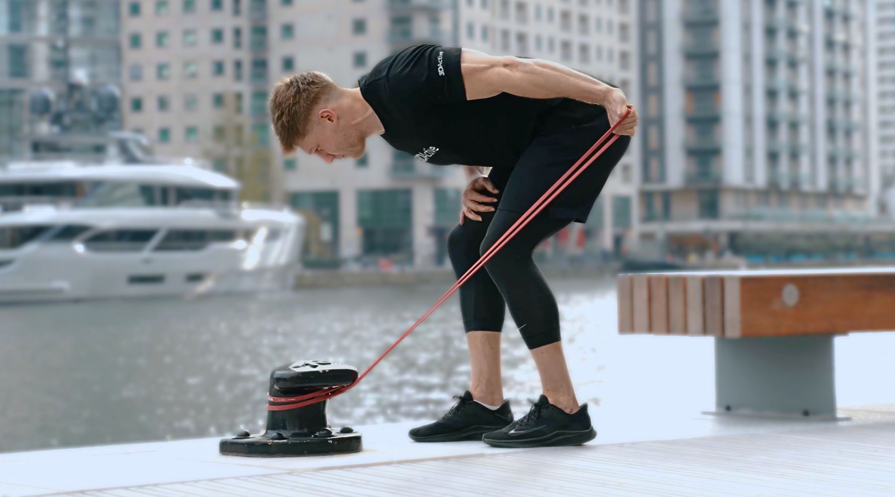 Young man strength training outdoors with red resistance band