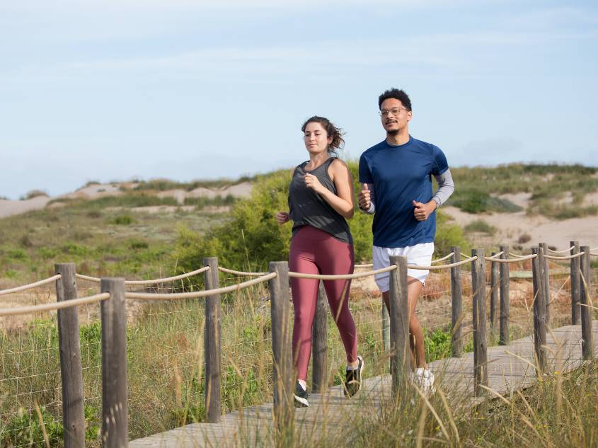 Young couple running on a beach walkway.