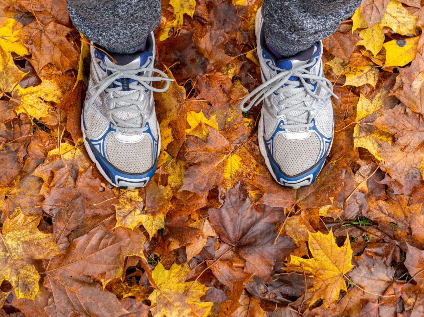 Overhead shot of person's athletic shoes on a road covered with fallen leaves.