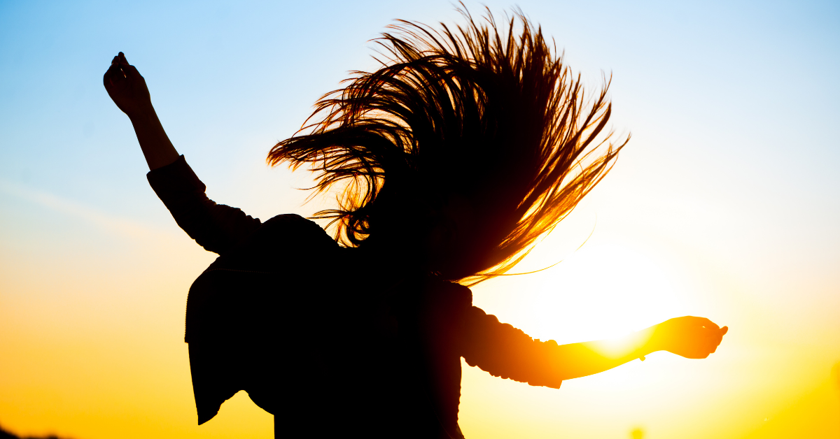 Silhouette of a woman jumping and flipping her hair against the sunset.