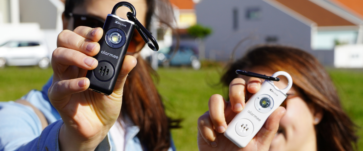 Two woman holding up an Alarmee Rechargeable Personal Safety Alarm in front of their faces.