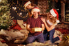 Family with Christmas hats on gathered on the living room floor around the dad opening a gift.
