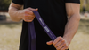 Muscular man in black t-shirt stretching a purple resistance band from 3DActive